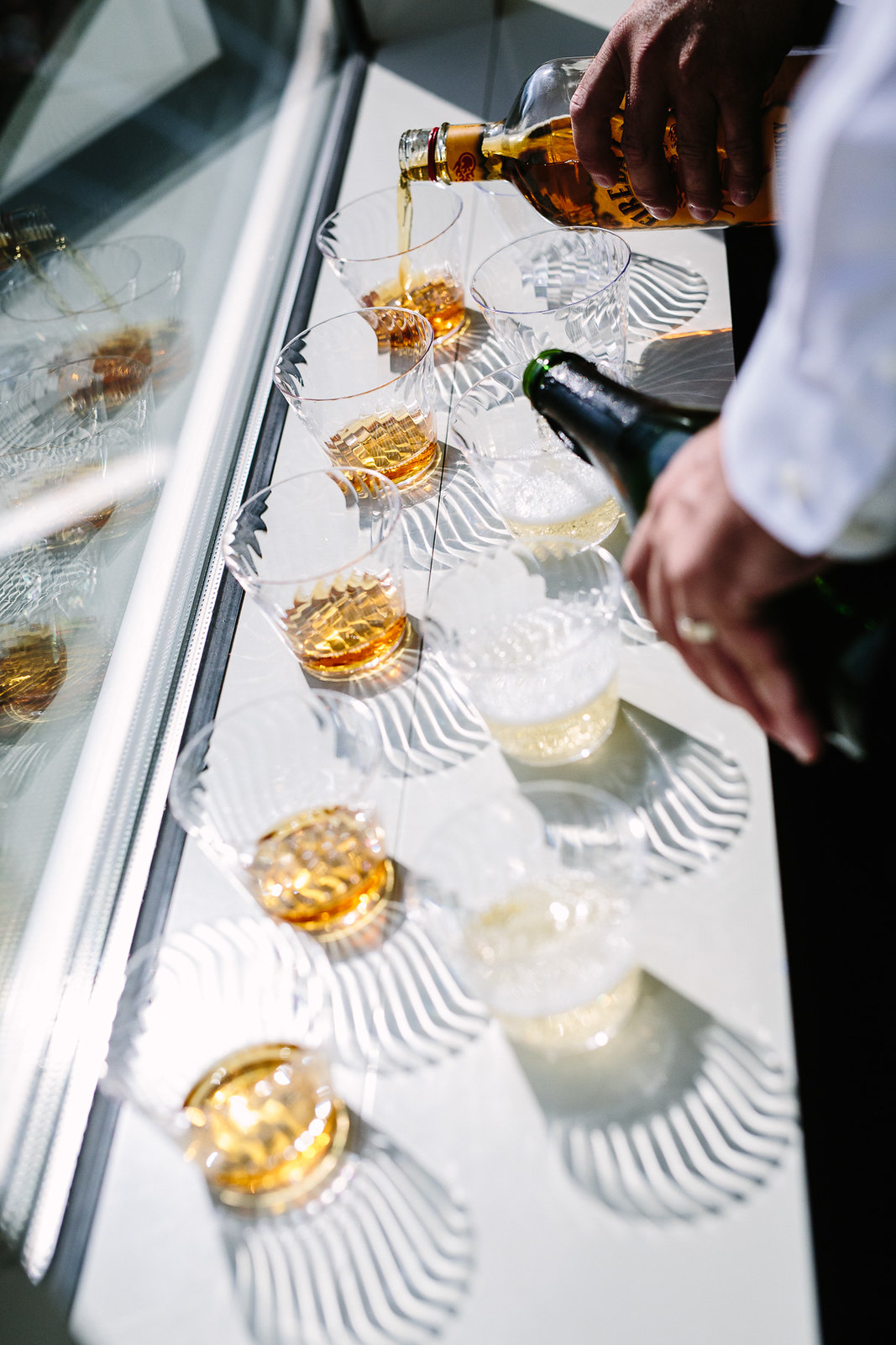 people pouring whiskey and champagne in clear plastic cups