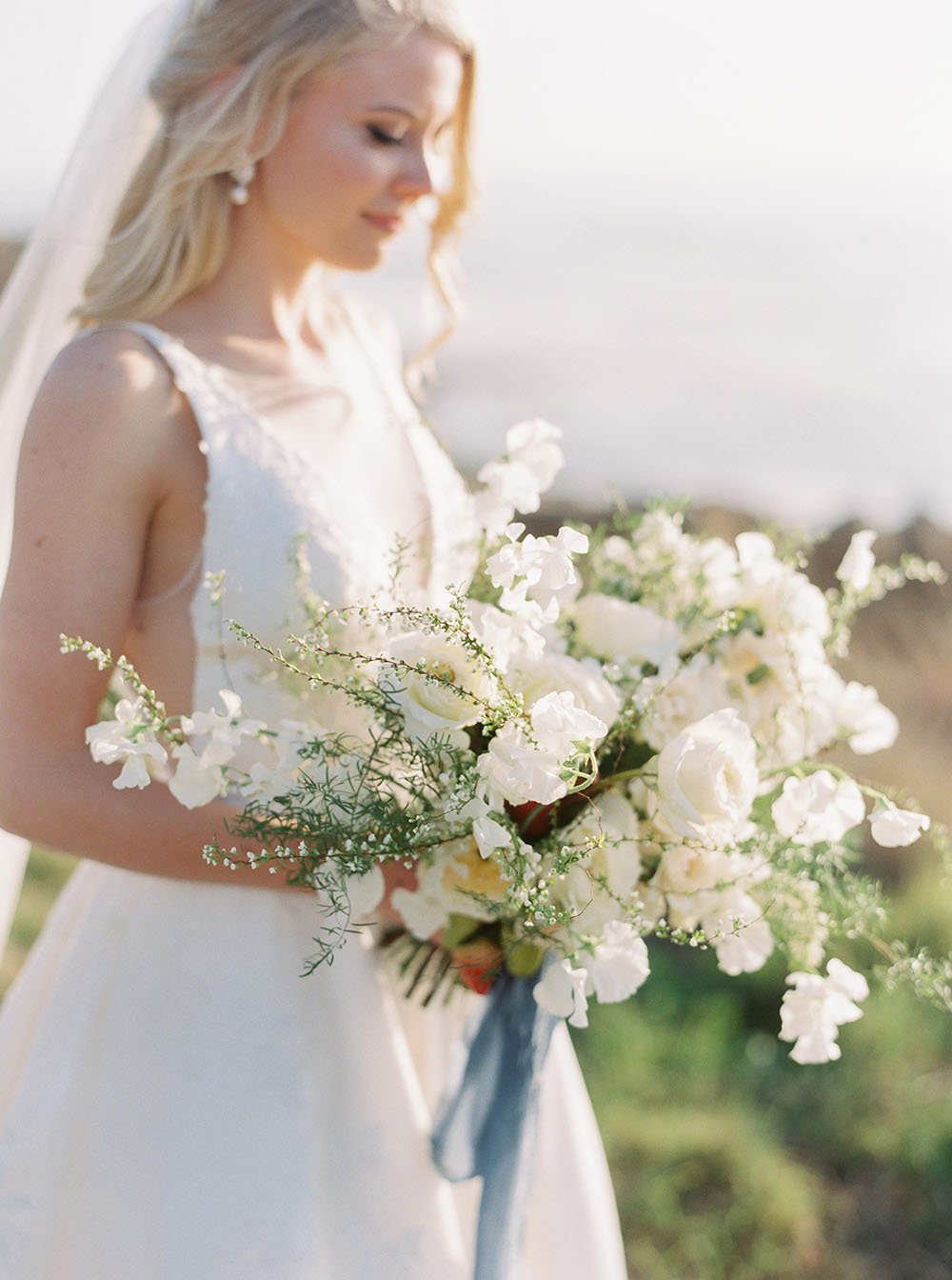 Chân dung cô dâu bỏ trốn ở Bờ biển Thái Bình Dương với bó hoa trắng hoang dã và dải ruy băng xanh bụi